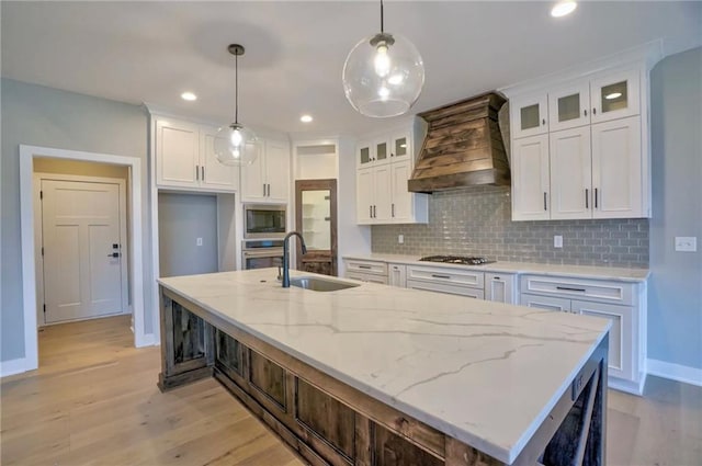 kitchen featuring a kitchen island with sink, sink, custom range hood, and white cabinets