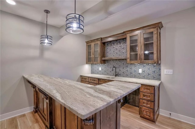 bar featuring light wood-type flooring, tasteful backsplash, decorative light fixtures, and sink