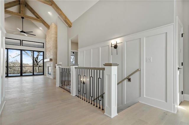 corridor featuring beam ceiling, a decorative wall, light wood-style flooring, an upstairs landing, and high vaulted ceiling