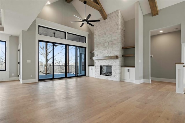 unfurnished living room with light wood finished floors, baseboards, a stone fireplace, high vaulted ceiling, and beam ceiling