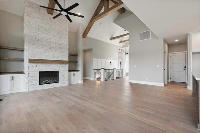 unfurnished living room featuring ceiling fan with notable chandelier, light wood finished floors, beamed ceiling, and visible vents