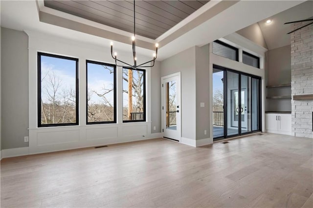 unfurnished dining area with a notable chandelier, wood finished floors, visible vents, baseboards, and a raised ceiling