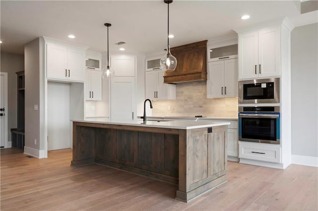 kitchen with built in microwave, custom exhaust hood, stainless steel oven, a sink, and light wood-type flooring