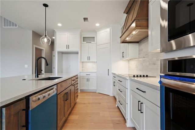 kitchen featuring appliances with stainless steel finishes, white cabinetry, a sink, light wood-type flooring, and premium range hood