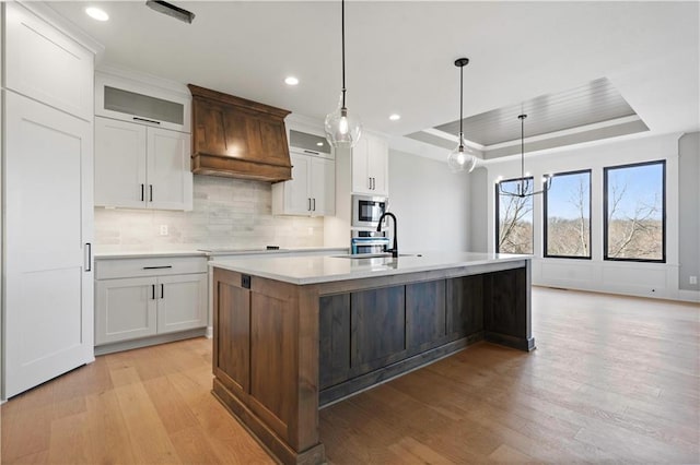 kitchen featuring a sink, light countertops, light wood-type flooring, a tray ceiling, and stainless steel microwave