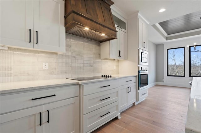 kitchen featuring stainless steel appliances, premium range hood, light wood-style floors, white cabinets, and decorative backsplash