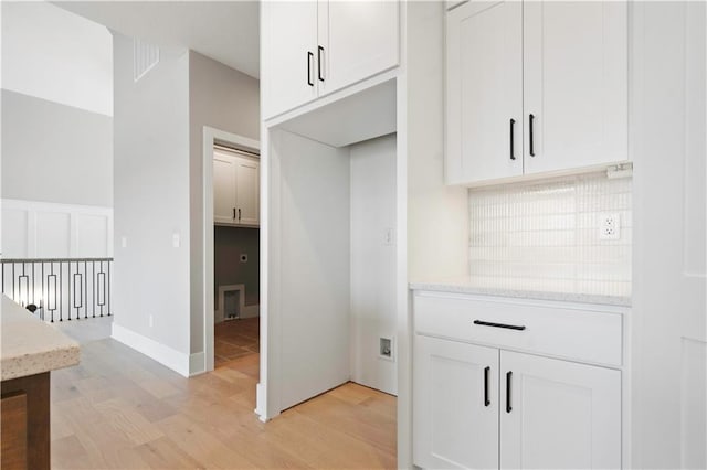 kitchen with tasteful backsplash, white cabinets, light wood-style flooring, and light stone countertops