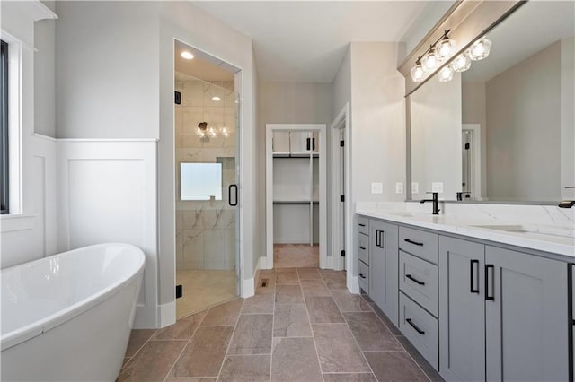 bathroom with a stall shower, a spacious closet, a freestanding tub, and vanity