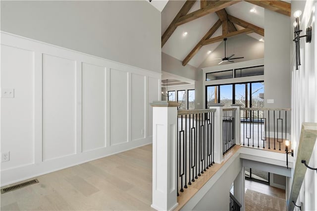 corridor with a decorative wall, wood finished floors, an upstairs landing, visible vents, and beam ceiling