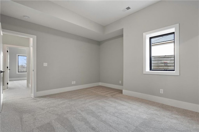 empty room featuring carpet floors, visible vents, plenty of natural light, and baseboards