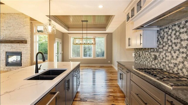 kitchen featuring a raised ceiling, hanging light fixtures, decorative backsplash, appliances with stainless steel finishes, and a sink