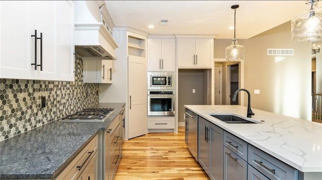 kitchen featuring visible vents, white cabinets, custom range hood, stainless steel appliances, and a sink