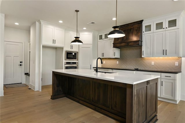 119 Teton Rdg, Lake Winnebago, MO 64034 - kitchen with appliances with stainless steel finishes, premium range hood, white cabinets, light wood-type flooring, and decorative backsplash