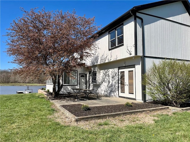 back of house with a water view, french doors, a patio area, and a lawn