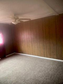 unfurnished room featuring ceiling fan, wood walls, and carpet floors