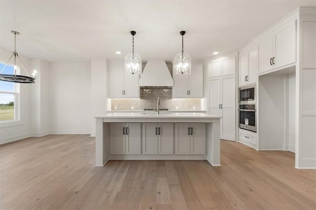 kitchen featuring tasteful backsplash, a center island with sink, light hardwood / wood-style floors, and custom exhaust hood