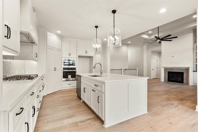 kitchen featuring white cabinets, light wood-type flooring, custom range hood, stainless steel appliances, and sink