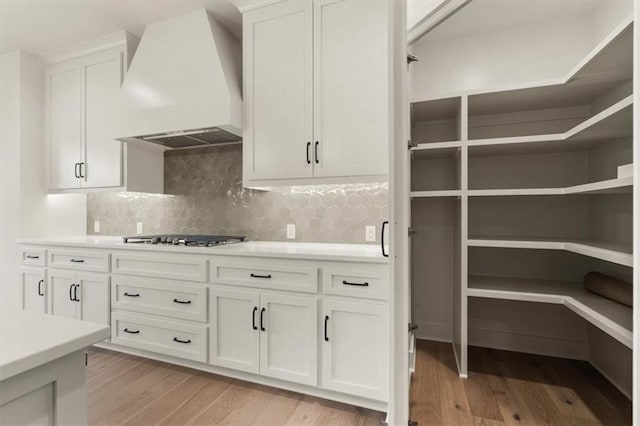 kitchen with backsplash, light wood-type flooring, white cabinetry, stainless steel gas cooktop, and custom range hood