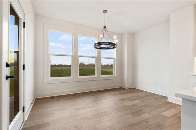 unfurnished dining area with a healthy amount of sunlight, an inviting chandelier, and light wood-type flooring