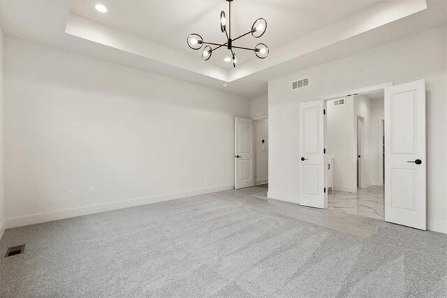 unfurnished bedroom featuring an inviting chandelier, light carpet, and a tray ceiling