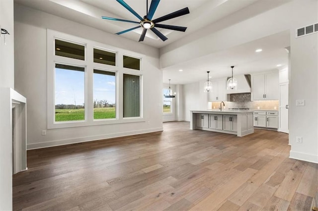 unfurnished living room featuring ceiling fan with notable chandelier, light hardwood / wood-style flooring, and sink