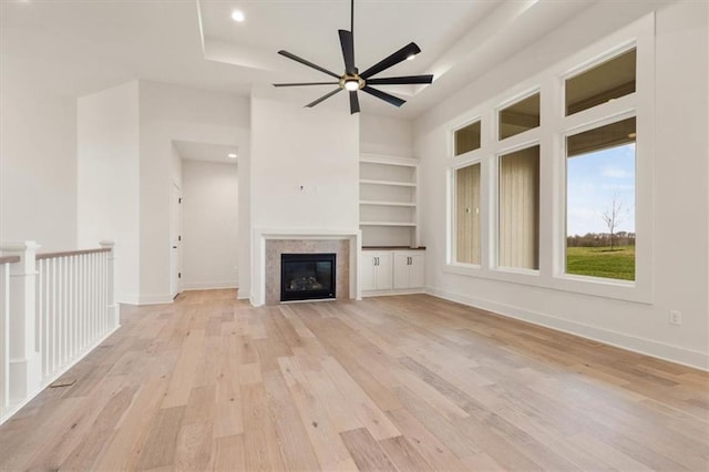 unfurnished living room with built in features, light hardwood / wood-style flooring, ceiling fan, and a tray ceiling