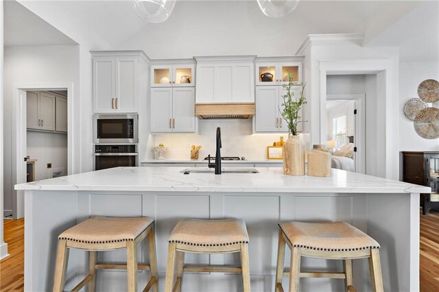 20132 Barker St, Spring Hill, KS 66083 - kitchen with stainless steel appliances, light wood-type flooring, light stone countertops, a kitchen island with sink, and a breakfast bar