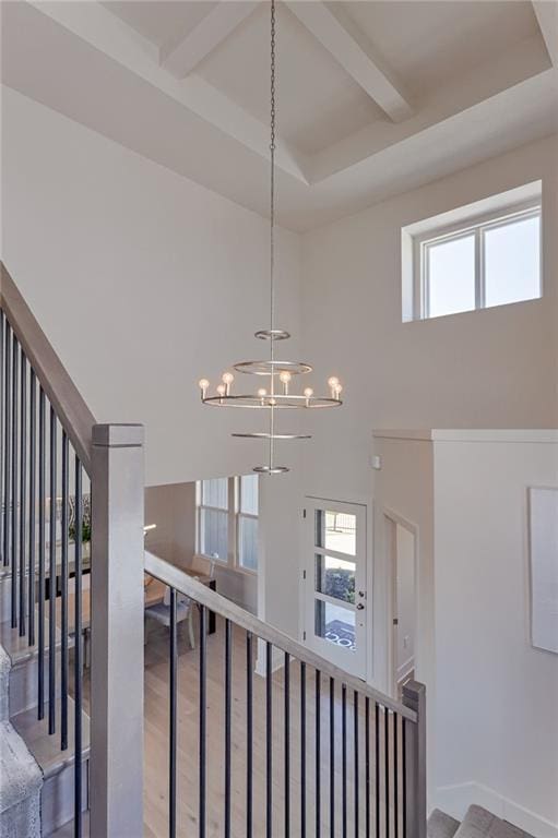 staircase featuring a notable chandelier, beam ceiling, wood-type flooring, and a towering ceiling