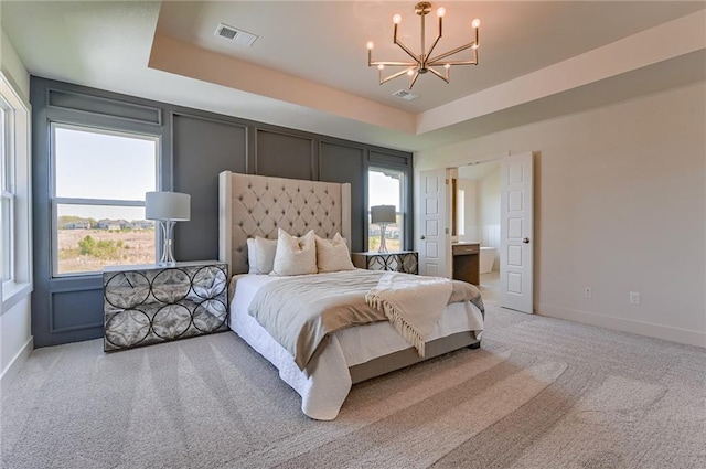 carpeted bedroom featuring connected bathroom, a raised ceiling, and a chandelier