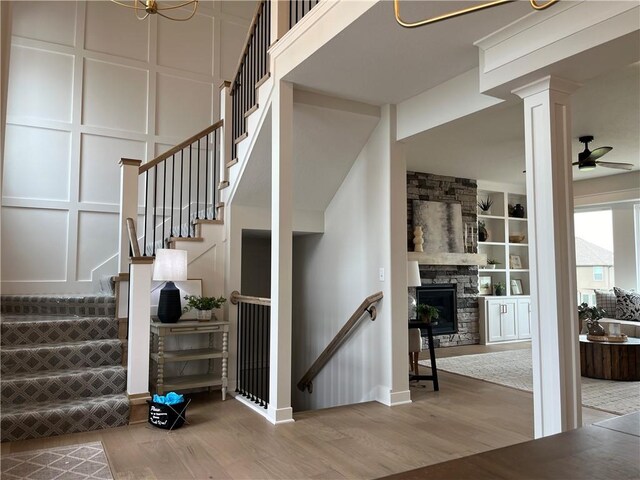 stairs with built in shelves, a stone fireplace, ceiling fan, and hardwood / wood-style flooring