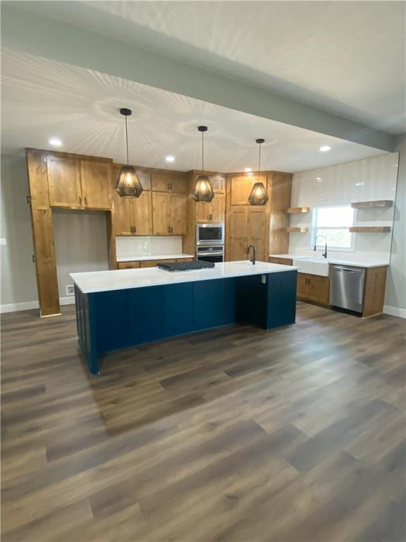 kitchen featuring a large island with sink, stainless steel appliances, decorative light fixtures, and dark hardwood / wood-style floors