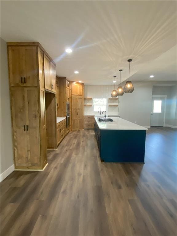 kitchen featuring dark hardwood / wood-style flooring, sink, hanging light fixtures, and an island with sink