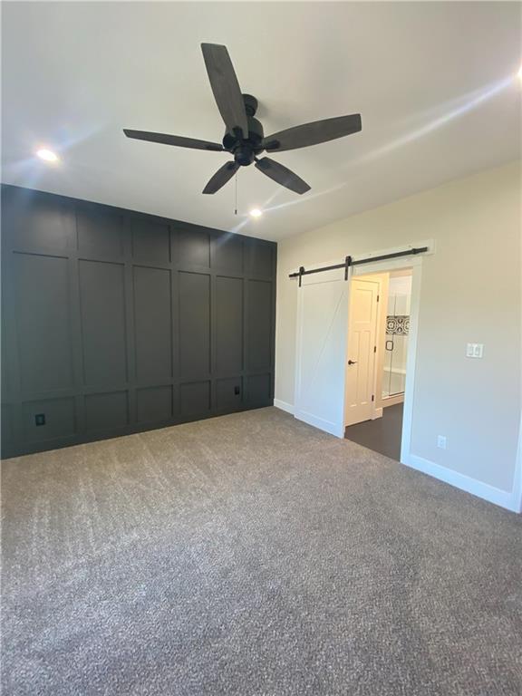 unfurnished bedroom featuring ceiling fan, dark colored carpet, and a barn door