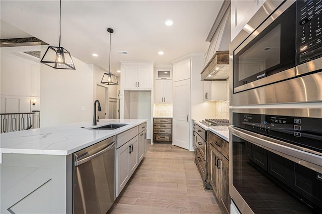 kitchen with tasteful backsplash, appliances with stainless steel finishes, light stone countertops, a kitchen island with sink, and a sink