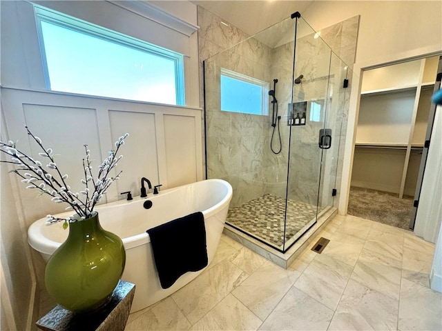 bathroom with a walk in closet, marble finish floor, a shower stall, and a freestanding tub