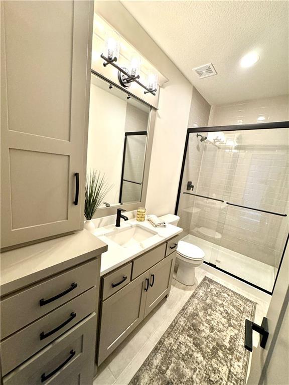 full bath featuring a stall shower, vanity, toilet, and a textured ceiling