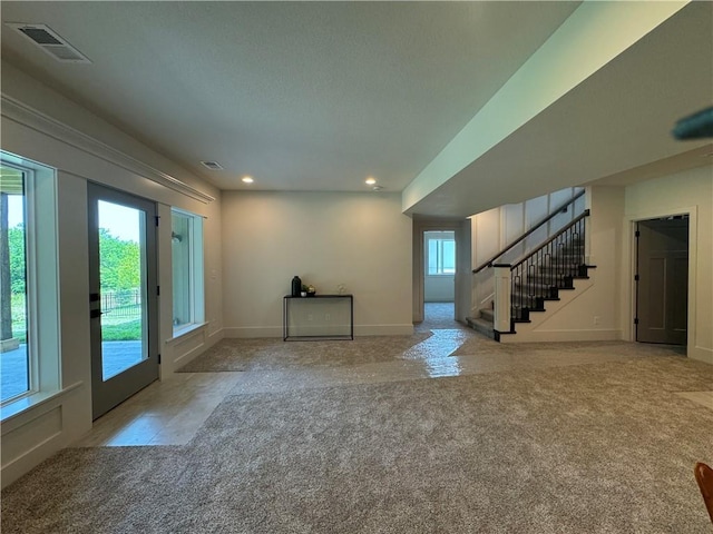 unfurnished living room featuring stairs, baseboards, visible vents, and light colored carpet