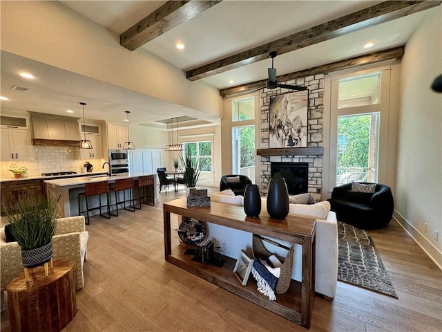 living room with light wood-style floors, beam ceiling, a fireplace, and baseboards