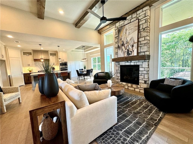 living area featuring a fireplace, recessed lighting, ceiling fan, light wood-type flooring, and beamed ceiling