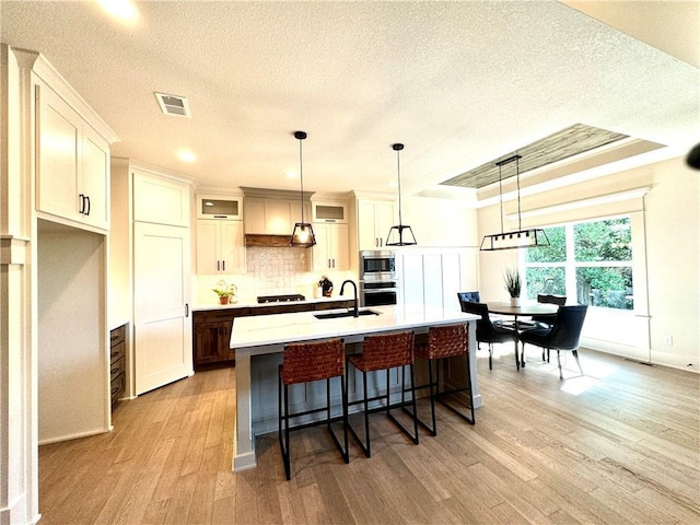 kitchen with stainless steel appliances, a sink, visible vents, light wood-style floors, and backsplash