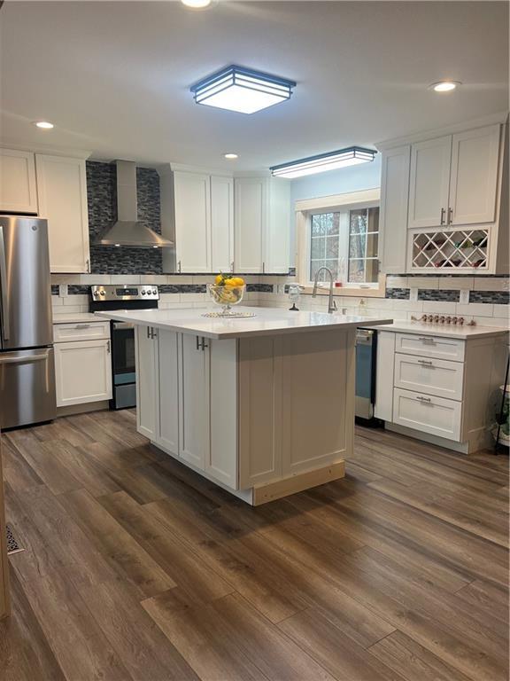 kitchen featuring dark hardwood / wood-style flooring, stainless steel appliances, white cabinets, wall chimney exhaust hood, and backsplash