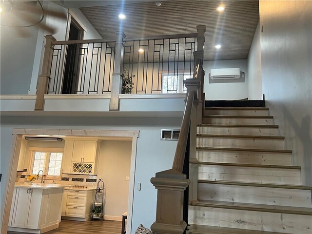 stairs with sink, hardwood / wood-style flooring, and a wall unit AC