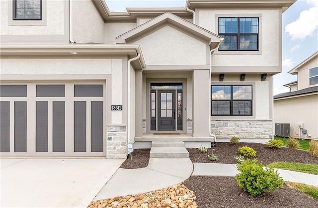 entrance to property with concrete driveway, stone siding, stucco siding, central AC unit, and a garage