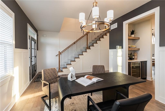 dining area with an inviting chandelier, stairway, wine cooler, light wood-style flooring, and a decorative wall