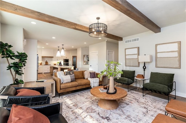 living area with beamed ceiling, recessed lighting, light wood finished floors, an inviting chandelier, and visible vents
