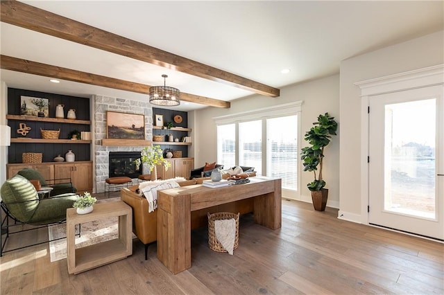 living room with hardwood / wood-style floors, an inviting chandelier, beamed ceiling, built in features, and a stone fireplace