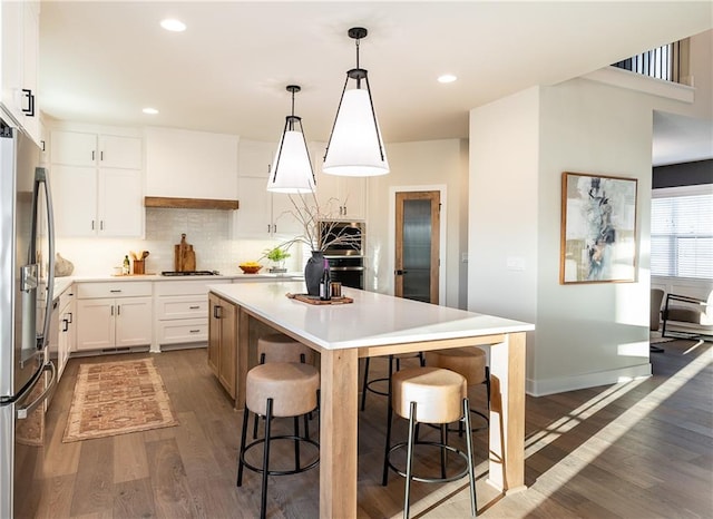 kitchen featuring hanging light fixtures, an island with sink, white cabinetry, stainless steel refrigerator, and dark wood-type flooring