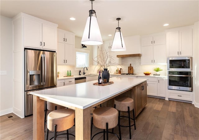 kitchen featuring stainless steel appliances, backsplash, white cabinetry, light countertops, and dark wood finished floors