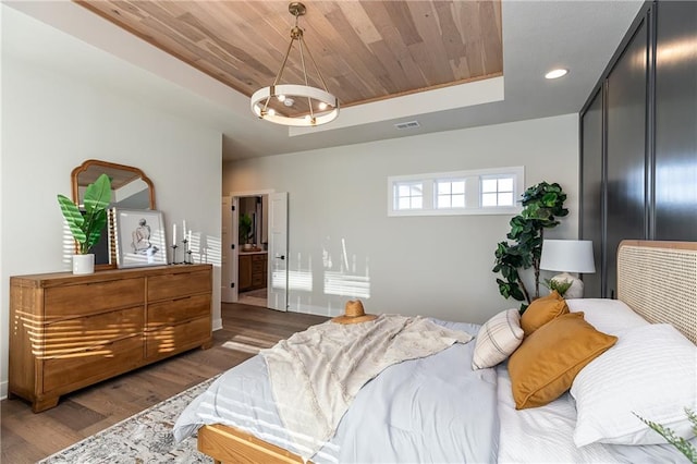 bedroom featuring connected bathroom, wood ceiling, dark hardwood / wood-style floors, an inviting chandelier, and a raised ceiling