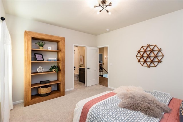 bedroom with ensuite bathroom, light colored carpet, and baseboards